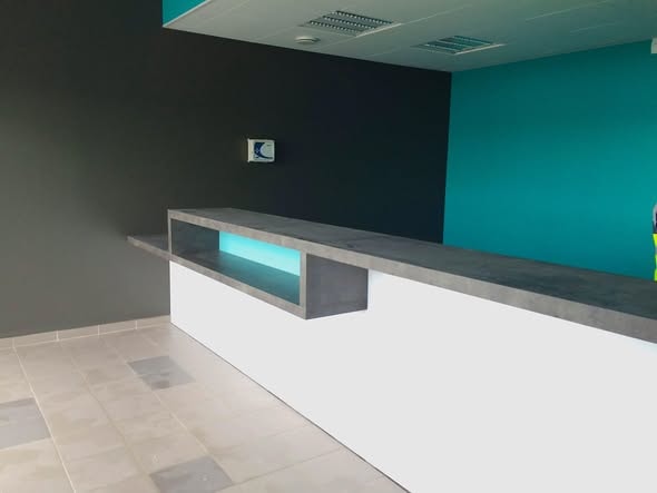 Comptoir d'accueil contemporain béton et LED bleue sur mur turquoise